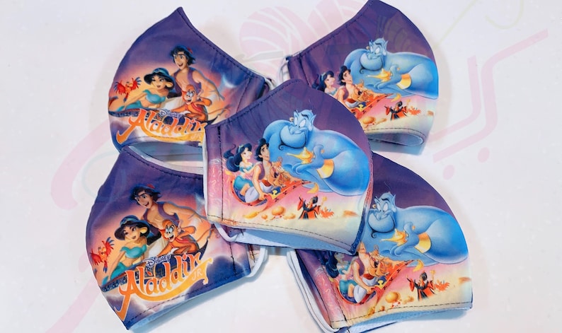 May include: Five purple and blue face masks featuring a Disney Aladdin theme. The masks depict images of Aladdin, Jasmine, Abu, and Genie. The masks are made from a soft, breathable fabric.