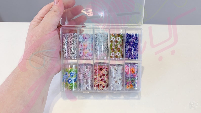 May include: A clear plastic storage box with 10 rolls of nail art transfer foil. The foil has various floral patterns in shades of pink, purple, blue, green, and white.