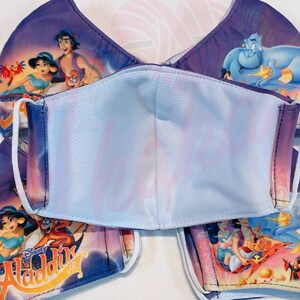 May include: A set of four purple and blue face masks featuring a printed image of Aladdin and Genie from the Disney film Aladdin. The masks have white elastic ear loops and a white inner layer.