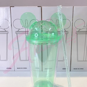 May include: A green plastic tumbler with a lid and a straw. The tumbler has two Mickey Mouse ears on the lid. The tumbler is labeled "450ML" and "MADE IN CHINA".