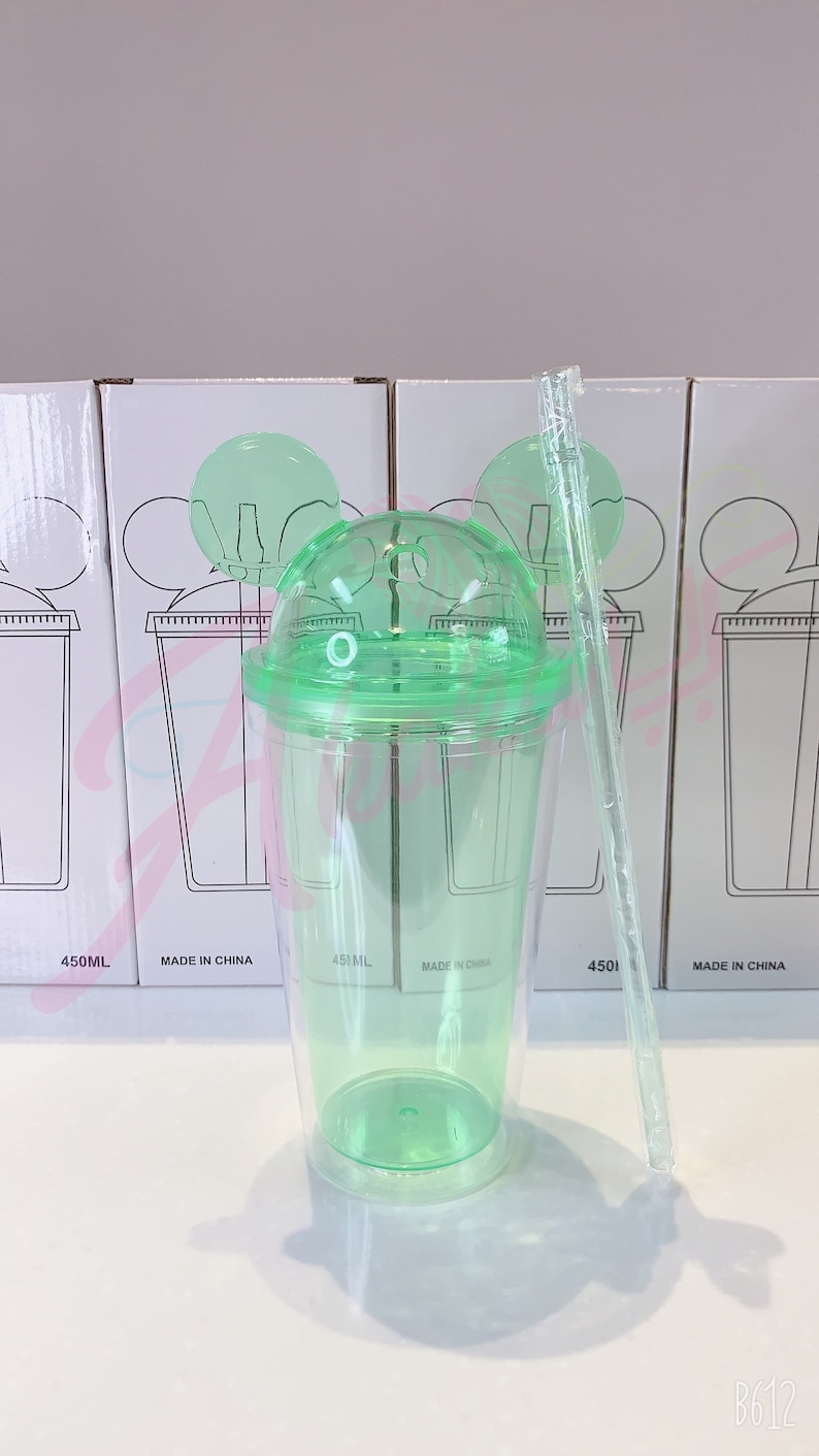 May include: A green plastic tumbler with a lid and a straw. The tumbler has two Mickey Mouse ears on the lid. The tumbler is labeled "450ML" and "MADE IN CHINA".