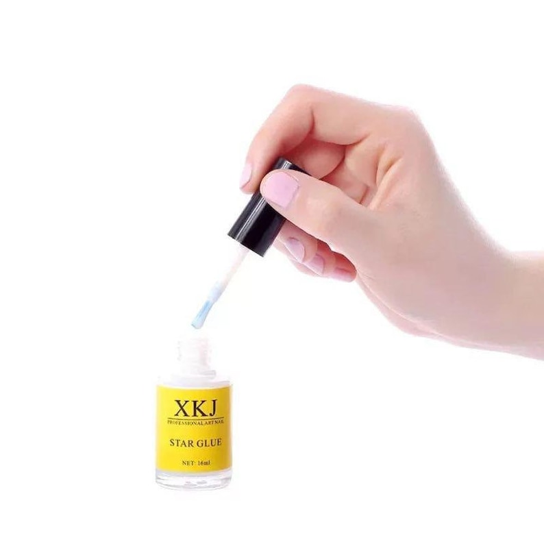 May include: A bottle of XKJ Star Glue with a yellow label and black cap. The bottle is held by a hand, with the applicator brush extended. The net volume is 16 ml.