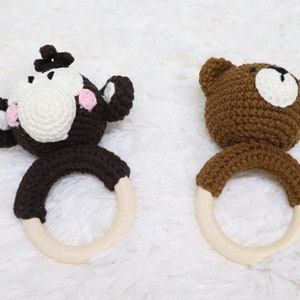 May include: Two crocheted baby teethers, one shaped like a monkey and the other shaped like a bear. Both teethers have wooden rings.