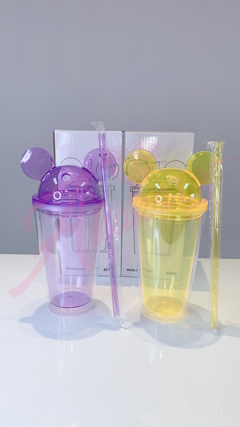 May include: Two clear plastic cups with lids and straws. The cups have a Mickey Mouse ear design on the lid. One cup is purple and the other is yellow. The cups are labeled "450ML" and "MADE IN CHINA".