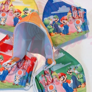 May include: Four colorful face masks featuring characters from the Super Mario Bros. video game franchise. The masks are made of fabric and have elastic ear loops. The characters on the masks include Mario, Luigi, Peach, Toad, and Yoshi.