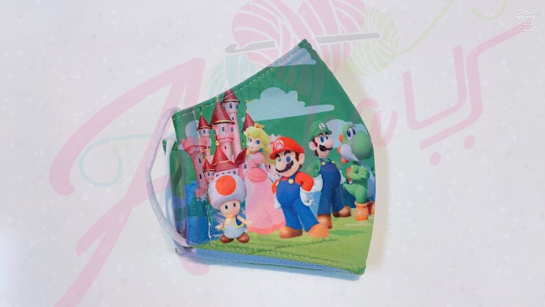 May include: A green, blue, pink, and white face mask with a cartoon image of Mario, Luigi, Peach, Toad, and Yoshi in front of a castle.