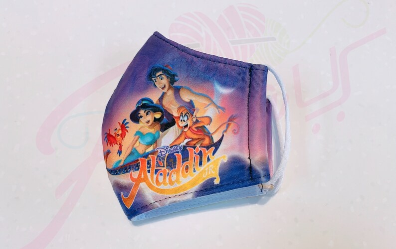 May include: A purple face mask with a Disney Aladdin Jr. design featuring Aladdin, Jasmine, and Abu on a magic carpet. The mask has white elastic ear loops.