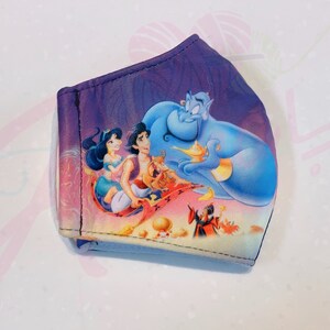 May include: A purple face mask featuring a printed image of Aladdin, Jasmine, and Genie flying on a magic carpet. The image also includes Jafar and Abu.