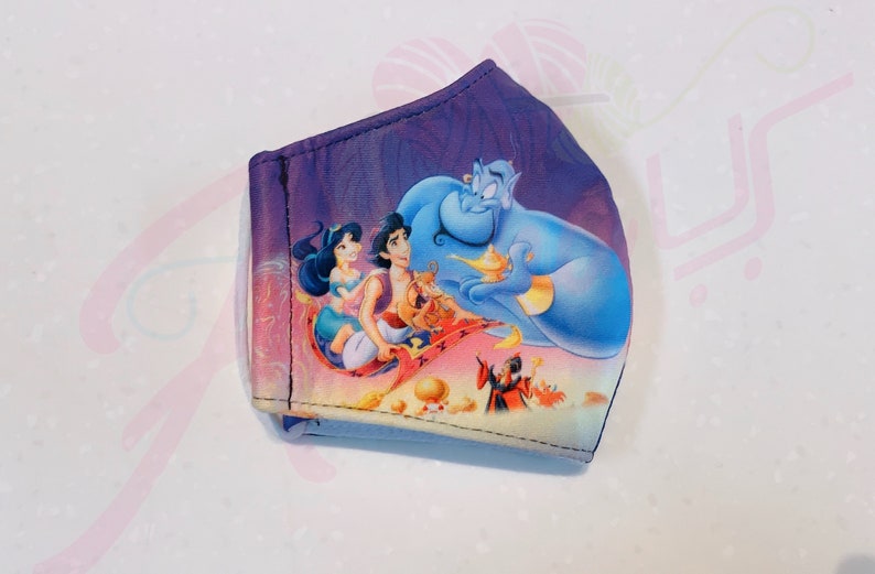 May include: A purple face mask featuring a printed image of Aladdin, Jasmine, and Genie flying on a magic carpet. The image also includes Jafar and Abu.