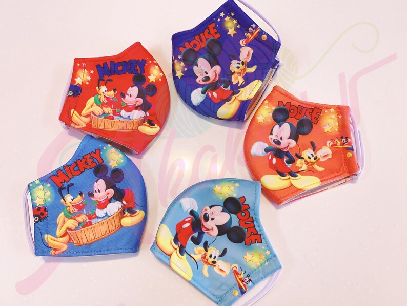 K&ouml;nnte beinhalten: Vier bunte Gesichtsmasken mit Mickey Mouse und Pluto. Die Masken sind aus Stoff und haben elastische Ohrschlaufen. Die Masken sind mit Sternen und den Worten "Mickey" und "Mouse" verziert.