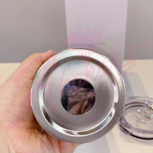 Puede incluir: La parte inferior de un vaso de acero inoxidable con una tapa plateada. El vaso tiene una abertura circular en la parte inferior.