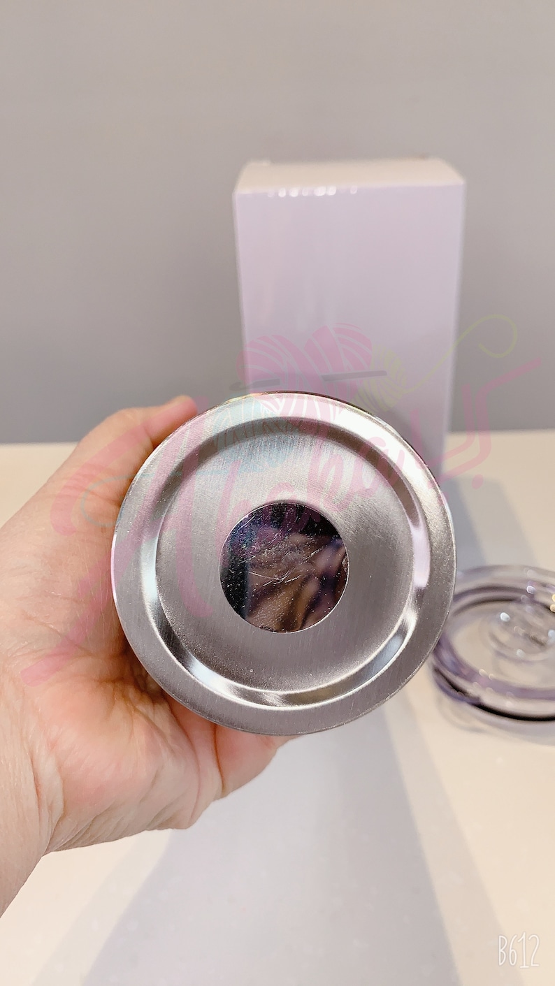Puede incluir: La parte inferior de un vaso de acero inoxidable con una tapa plateada. El vaso tiene una abertura circular en la parte inferior.