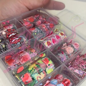 以下が含まれることがあります： 透明なプラスチック製の箱に、ネイルアート用のホイルのロールが詰められています。ホイルには、ハート、花、唇、そして「love」という言葉など、さまざまなデザインが施されています。