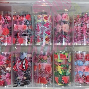 以下が含まれることがあります： ピンクと白のパターンが施されたネイルアートホイルが10ロール入った透明なプラスチック製の収納ボックス。パターンには、ハート、唇、花、そして「love」という言葉が含まれています。