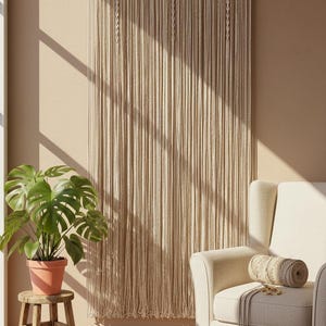 May include: A large off-white macrame wall hanging featuring intricate knotted patterns at the top and long, flowing vertical fringe strands suspended from a horizontal wooden rod, creating a textured fiber art display on a wall.