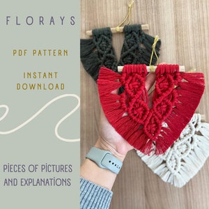 Könnte beinhalten: Drei Makramee-Wandbehänge in Rot, Grün und Creme. Jeder Behang hat die Form eines Herzens mit Fransen. Die Behänge sind an Holzleisten befestigt.