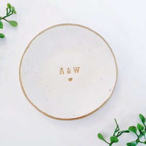 May include: White ceramic ring dish with a gold rim and the initials "A & W" with a small heart in between.
