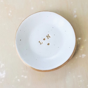 May include: White ceramic ring dish with a gold rim. The dish has the letters "L" and "N" with two small hearts in between.
