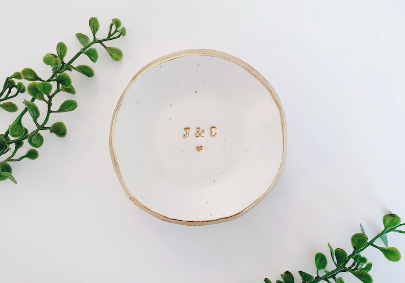 May include: White ceramic ring dish with a gold rim and the initials "J & C" in gold lettering. A small gold heart is centred below the initials.