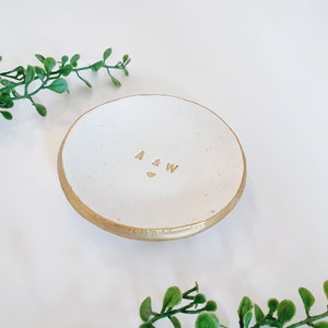 May include: White ceramic ring dish with a gold rim and the initials "A & W" inscribed in gold lettering.