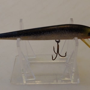 May include: A black and silver fishing lure with a yellow mouth and two treble hooks.