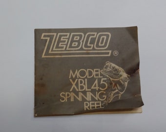Puede incluir: Un manual de instrucciones de carrete de spinning Zebco marrón y blanco con el número de modelo XBL45 impreso en él. El manual presenta una ilustración en blanco y negro de un pez.