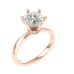 Puede incluir: Anillo de compromiso de oro rosa con una gema grande, redonda y transparente. El anillo presenta un engaste clásico de seis puntas y una banda delicada. Pequeñas piedras de acento alrededor de la base de la piedra principal.