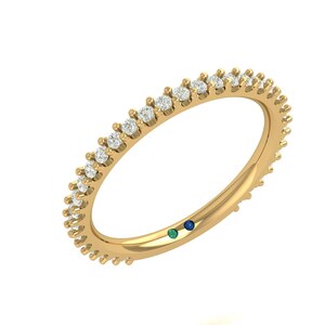 May include: A gold ring with a band of small, clear gemstones. The ring has a smooth, polished finish and a small green and blue gemstone detail. The ring is set against a white background.