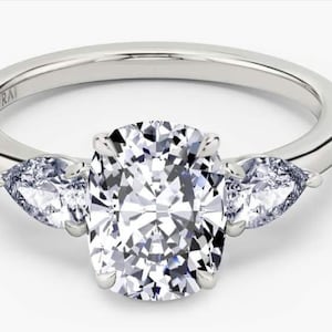 Könnte beinhalten: Platinring mit einem großen, oval geschliffenen Diamanten als Mittelstein und zwei birnenförmigen Seitensteinen. Der Ring hat ein poliertes Band und ein klassisches Design. Der Markenname "VRAI" ist auf dem Band eingraviert.