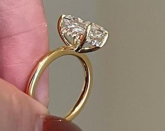 May include: A gold ring featuring a large, clear, oval-cut gemstone. The ring's band is polished gold, and the gemstone is secured by delicate prongs. The ring is held by a person's finger.