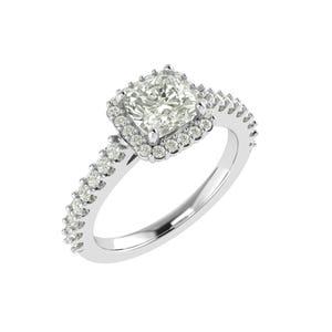 Puede incluir: Un anillo de compromiso plateado con una piedra central de corte cuadrado rodeada por un halo de piedras más pequeñas. La banda también está adornada con pequeñas piedras brillantes. El anillo se presenta sobre un fondo blanco.