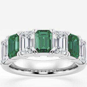 Puede incluir: Un anillo de plata con cinco piedras preciosas de talla esmeralda. El anillo alterna entre esmeraldas verdes vibrantes y piedras blancas claras y brillantes. El engaste es de diseño clásico y elegante.