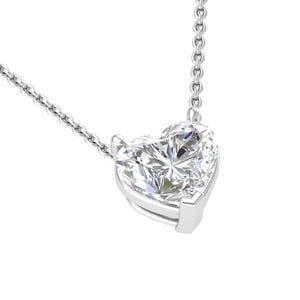 Puede incluir: Un collar de plata con un colgante de diamante en forma de corazón. El diamante está facetado, reflejando la luz, y engastado en un bisel de plata. La cadena es un diseño delicado y enlazado, adecuado para el uso diario.