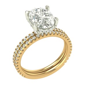 Puede incluir: Un anillo de oro con un gran diamante central de talla ovalada. La banda también es de oro y presenta dos filas de diamantes más pequeños. El anillo se muestra sobre un fondo blanco, resaltando su brillo y diseño.