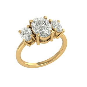 Puede incluir: Un anillo de oro con tres diamantes de talla ovalada. El diamante central es más grande que las dos piedras laterales. El anillo tiene un diseño clásico y elegante, con los diamantes engastados en garras. La banda es lisa y pulida.