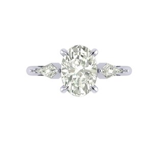 Puede incluir: Un anillo de compromiso plateado con una piedra central de corte ovalado y dos piedras laterales en forma de pera. El anillo se muestra sobre un fondo blanco, resaltando el brillo de las piedras preciosas.