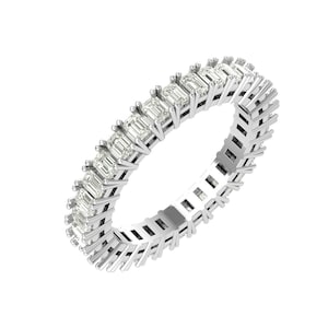 Puede incluir: Un anillo de eternidad plateado con una fila continua de piedras preciosas de talla esmeralda. La banda del anillo es de plata y tiene un diseño geométrico. Las piedras preciosas son claras y reflejan la luz. Esta es una joya.