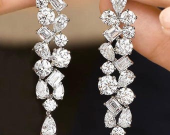 May include: Elegant dangle earrings featuring a cascade of sparkling white diamonds. The earrings showcase a variety of diamond cuts, including round, pear, and emerald shapes, set in a silver or white gold setting. The design is symmetrical and eye-catching.