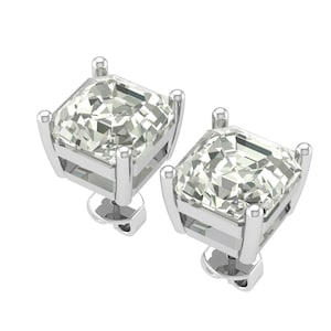 Puede incluir: Un par de pendientes de diamantes con corte cuadrado. Cada pendiente presenta un diamante grande, transparente y facetado engastado en una montura de plata o oro blanco. Los pendientes se muestran sobre un fondo blanco.