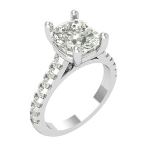 Puede incluir: Un anillo de compromiso plateado con un gran diamante central de talla cuadrada. La banda está adornada con diamantes más pequeños. El anillo se presenta sobre un fondo blanco, resaltando su brillo y diseño.