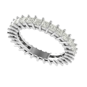 Puede incluir: Un anillo de eternidad plateado con una fila continua de piedras preciosas claras de talla cuadrada. La banda del anillo está detallada con pequeñas barras verticales, creando una apariencia texturizada. Las piedras preciosas están engastadas juntas, formando un círculo completo.