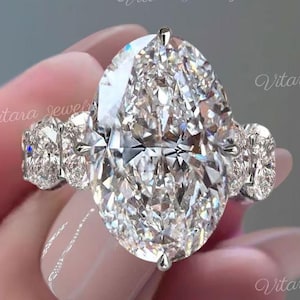 Puede incluir: Un deslumbrante anillo de diamantes con una gran piedra central de talla ovalada flanqueada por dos diamantes rectangulares más pequeños. El engaste del anillo es plateado. Una fina joya.