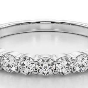 Könnte beinhalten: Ein silberner Bandring mit mehreren runden Diamanten. Die Diamanten sind gleichmäßig angeordnet und funkeln hell. Der Ring ist ein klassisches Design, geeignet für verschiedene Anlässe.