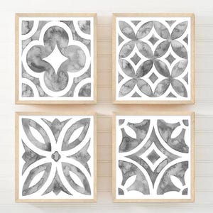 May include: Four framed watercolor prints with geometric patterns in shades of gray and white. Each print has a light wood frame. The patterns include floral and geometric designs, creating a cohesive set for wall decor.
