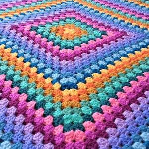 May include: A colourful crocheted blanket with a rainbow pattern. The blanket is made with a variety of different coloured yarns, creating a vibrant and eye-catching design.