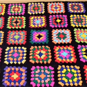 May include: A colorful crochet blanket with a black background. The blanket is made up of many squares, each with a different pattern of colorful yarn.
