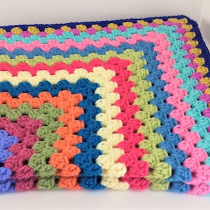 May include: A colorful crocheted blanket with a rainbow pattern and a blue border.