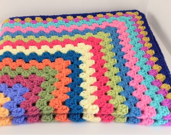 May include: A colorful crocheted blanket with a rainbow pattern and a blue border.