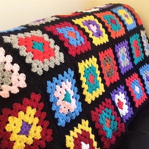 May include: A colorful crocheted blanket with a black background and squares of various colors, including red, yellow, blue, green, and purple.