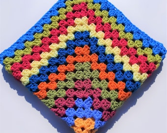 May include: A colorful, square-shaped crochet blanket. The blanket features a vibrant granny square design with a palette of blue, green, red, orange, and yellow. The crochet stitches are clearly visible, showcasing the handmade quality of the item.